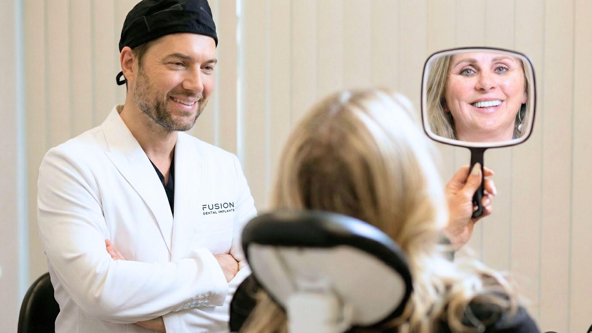 Dr. Antipov with patient admiring her new smile in mirror at Fusion Dental Implants