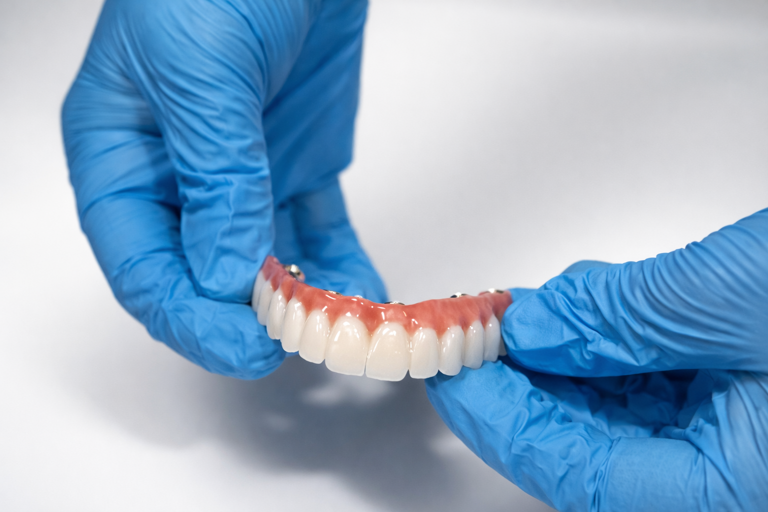 Gloved hands holding a full-arch zirconia prosthetic backed by lifetime warranty